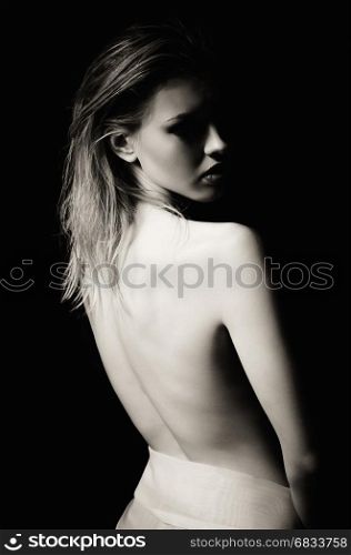 Dramatic portrait of a sad young woman among the dark. Rear view, black and white