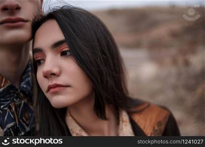 Dramatic portrait of a young brunette girl and a guy in cloudy weather.the girl leaned over the boy&rsquo;s shoulder. selective focus, small focus area