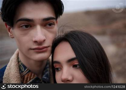 Dramatic portrait of a young brunette girl and a guy in cloudy weather.the girl leaned over the boy&rsquo;s shoulder. selective focus, small focus area