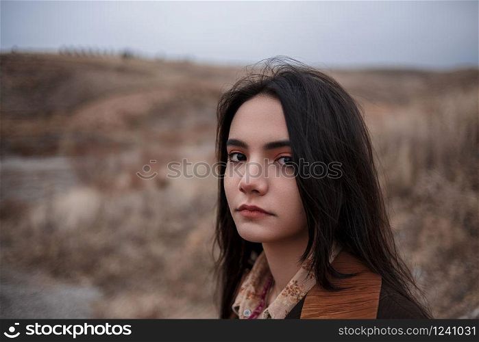 Dramatic portrait of a young brunette girl in cloudy weather against the background of mountains. selective focus, small focus area