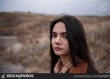 Dramatic portrait of a young brunette girl in cloudy weather against the background of mountains. selective focus, small focus area