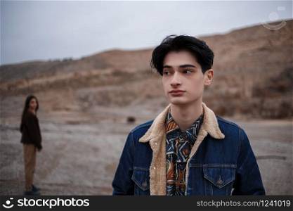 Dramatic portrait of a young brunette guy in cloudy weather. somewhere behind him, out of focus, his beloved leaves him . selective focus, small focus area