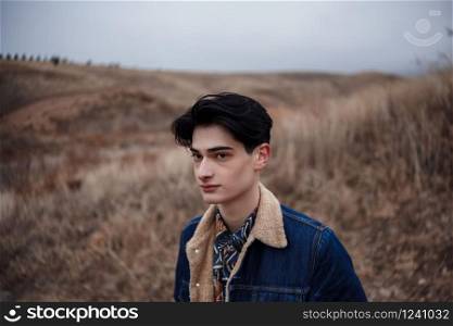 Dramatic portrait of a young brunette guy in cloudy weather against the background of mountains. selective focus, small focus area