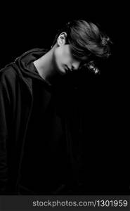 dramatic portrait of a young guy in a black hoodie on a black background. black and white photo