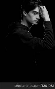 dramatic portrait of a young guy in a black hoodie on a black background. black and white photo