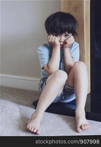 Dramatic portrait of little boy sitting on the floor with scared face, Sad Child covered face with his hands and looking down with worrying face, Stressed child. Domestic Family violence and aggression concept violence.