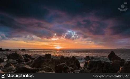 Dramatic sea sunset on rock shore with waves