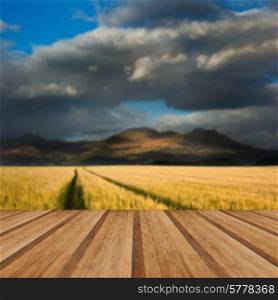 Dramatic sky over landscape of mountain range with corn field in foreground with wooden planks floor