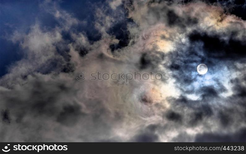 Dramatic sky with some dark and many white clouds covering the sun and making it semi-transparent, abstract or background