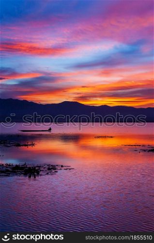 Dramatic sunset sky over the lake and mountains in the backgrounds. Colourful clouds and sky reflection on the lake. Fisherman fishing on the boat. Phayao Lake, Thailand.