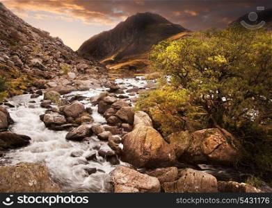 Dramatic sunset with beautiful sky over mountain range giving a strong moody landscape wiht flowing waterfall in foreground