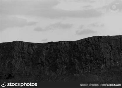 Dramatic view in black and white of the Arthur&rsquo;s Seat volcanic rock hills and two unidentifiable people in Edinburgh, Scotland