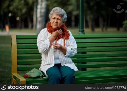 Dranny in scarf leisures on the bench in summer park. Aged people lifestyle. Pretty grandmother having fun outdoors, old female person on nature. Dranny in scarf leisures on bench in summer park