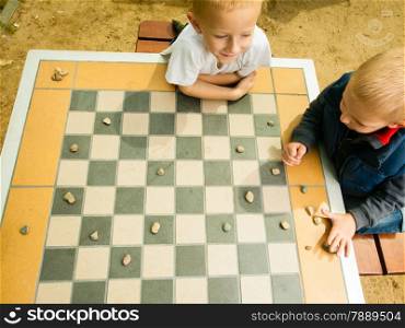 Draughts board game. Little boys clever children kids playing checkers thinking, outdoor in the park. Childhood and development