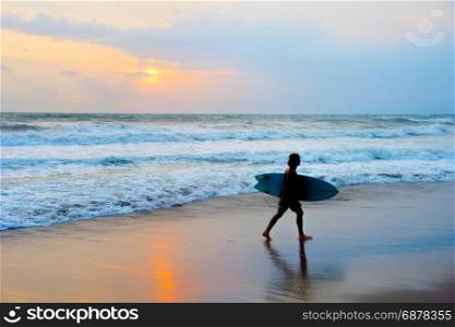 Dreadlocks surfer on the beach with surfboard at sunset. Bali island