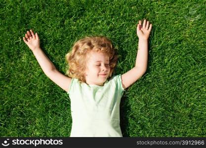 Dreaming adorable little girl lying on grass, top view