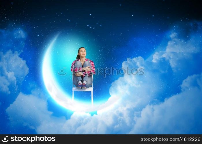Dreaming at night. Young pretty girl sitting on moon in sky