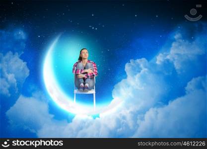 Dreaming at night. Young pretty girl sitting on moon in sky