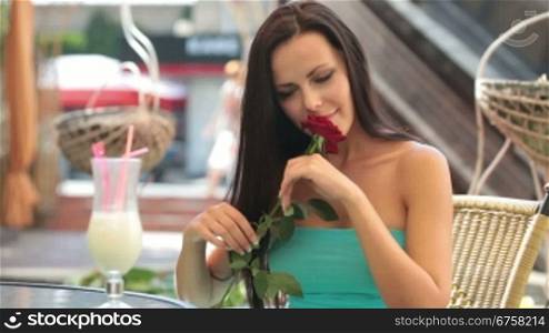 dreaming lady with a rose in hand, sitting in a restaurant