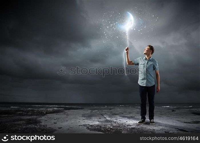 Dreaming man. Young man holding moon balloon against dark background
