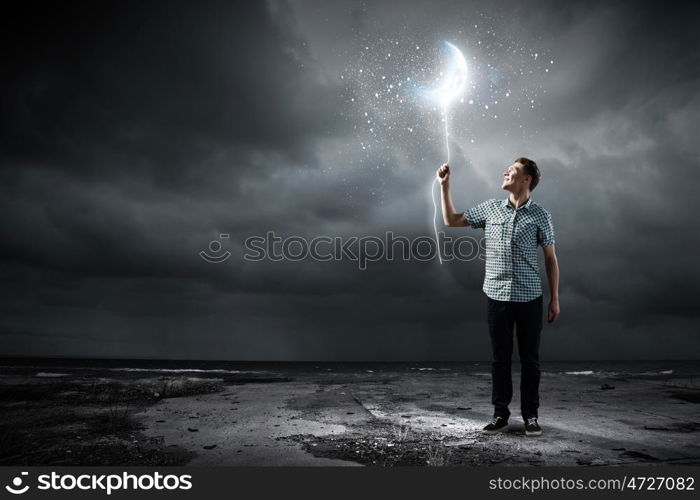 Dreaming man. Young man holding moon balloon against dark background