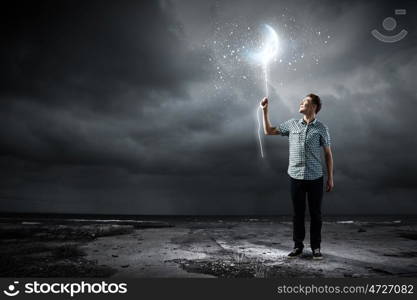 Dreaming man. Young man holding moon balloon against dark background