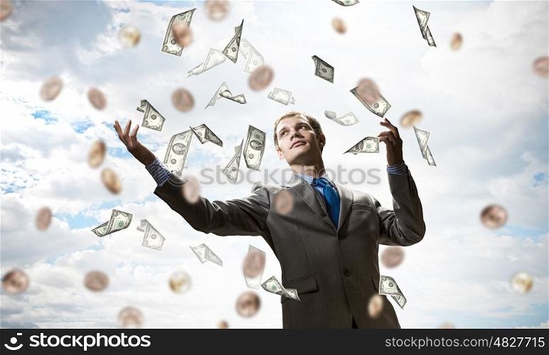 Dreaming to become rich. Young businessman standing in the rain of money banknotes
