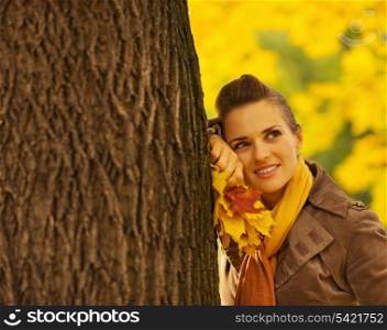 Dreaming woman with fallen leaves leaning against tree