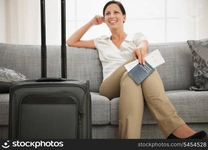 Dreaming woman with passport and air ticket sitting on couch