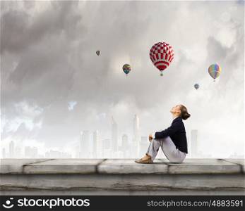 Dreaming woman. Young pretty lady sitting on top of building and dreaming