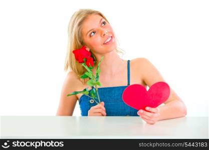Dreaming young girl sitting at table with rose and Valentine heart&#xA;