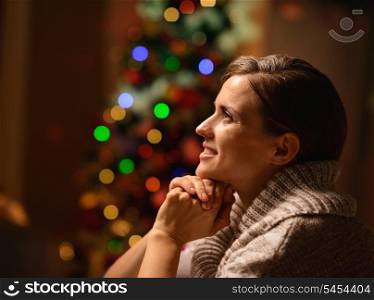 Dreaming young woman sitting chair in front of Christmas tree