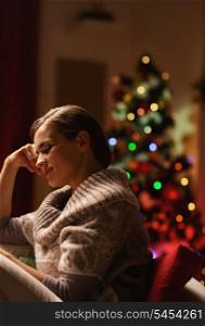 Dreaming young woman sitting in armchair in front of christmas tree