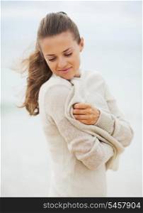 Dreaming young woman wrapping in sweater on coldly beach