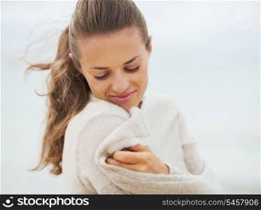 Dreaming young woman wrapping in sweater on coldly beach