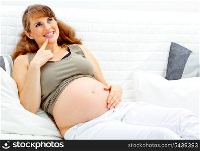 Dreams beautiful pregnant woman sitting on sofa at home and holding her belly&#xA;