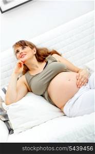 Dreams beautiful pregnant woman sitting on sofa at home and holding her belly&#xA;
