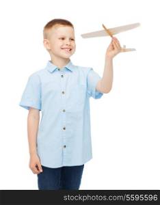 dreams, future, hobby and childhood concept - smiling little boy holding a wooden airplane model in his hand