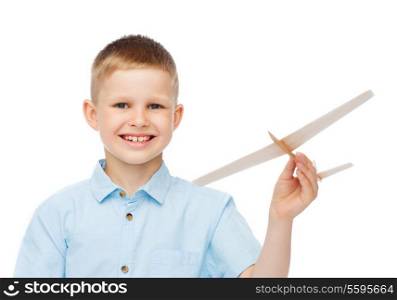 dreams, future, hobby and childhood concept - smiling little boy holding a wooden airplane model in his hand