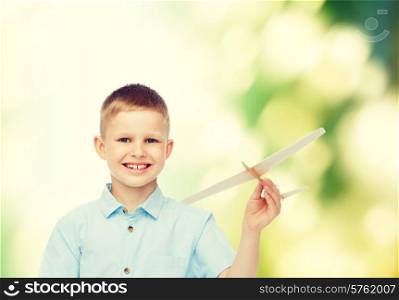 dreams, future, hobby, ecology and childhood concept - smiling little boy holding wooden airplane model in his hand over green background