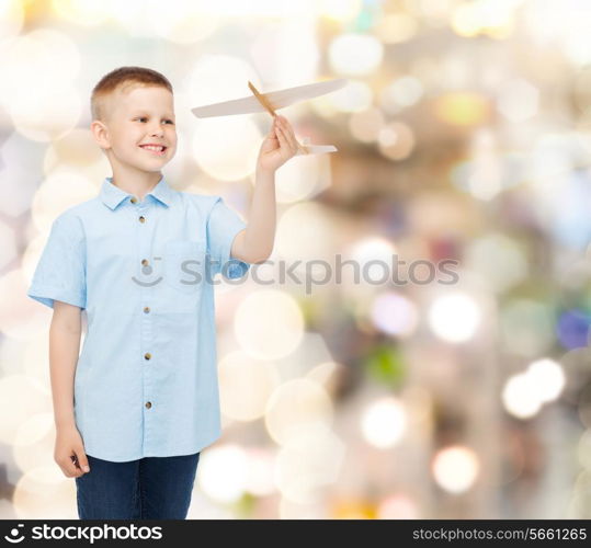 dreams, future, hobby, holidays and childhood concept - smiling little boy holding wooden airplane model in his hand over sparkling background