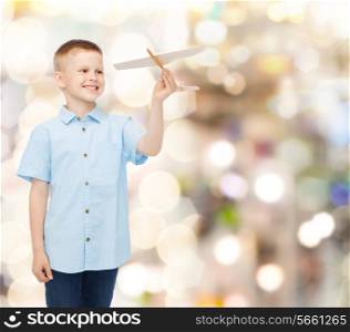 dreams, future, hobby, holidays and childhood concept - smiling little boy holding wooden airplane model in his hand over sparkling background