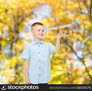 dreams, future, hobby, season and childhood concept - smiling little boy holding wooden airplane model in his hand over autumn park background