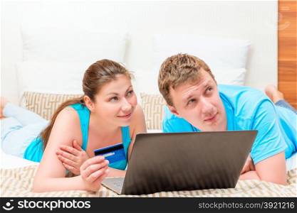 dreamy couple in bed with a credit card and laptop