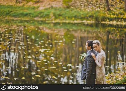 Dreamy portrait of the newlyweds on the shore of a forest lake in autumn.. The couple dream of the future standing on the shore of fall lake 202.