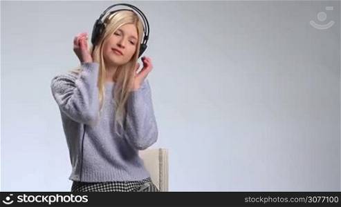 Dreamy teenage girl with headphones singing song over white. Young attractive woman with closed eyes wearing earphones, touching earcups with both hands and slowly swaying along the beautiful song.