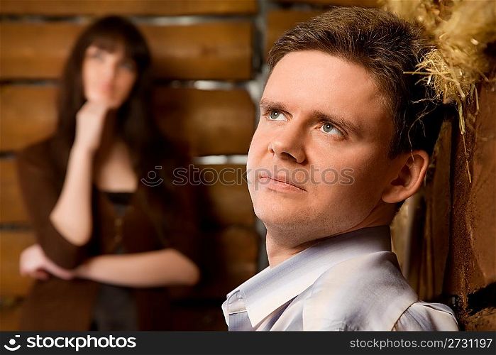 dreamy young man and young woman in wooden log hut, woman standing near wall on background