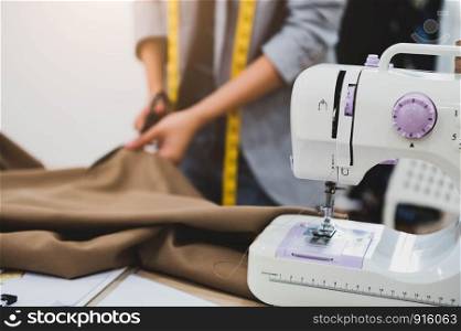 Dressmaker cutting dress fabric on sketch line with sewing machine foreground. Fashion designer tailor or sewer in workshop studio designing new collection clothes. Business owner and entrepreneur