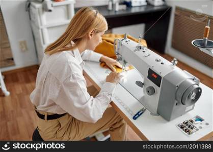 Dressmaker sews cloth on sewing machine at her workplace in workshop. Dressmaking occupation, handmade tailoring business, handicraft hobby. Dressmaker sews cloth on sewing machine, workshop