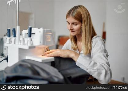 Dressmaker sews cloth on sewing machine at her workplace in workshop. Dressmaking occupation, handmade tailoring business.. Dressmaker sews cloth on sewing machine, workshop